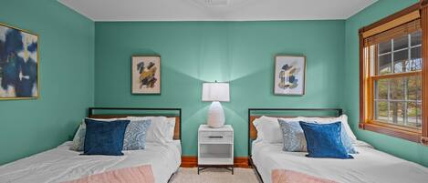 A bedroom with two beds, a ceiling fan, a window, and artwork on the walls.