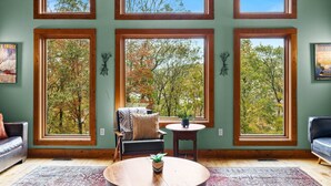 A room with large windows, a sofa, a chair, a small table, and a rug. - Fam-friendly Cabin Mins 2 Beach Ski w Hot Tub (Lake Harmony)