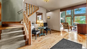 A staircase with wooden railings, a round table with chairs, and a view of the outdoors through large windows. - Fam-friendly Cabin Mins 2 Beach Ski w Hot Tub (Lake Harmony)