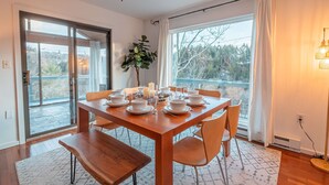 A dining area with a wooden table set for four, a potted plant, and a view through large windows. - Riverfront Dog Friendly Cabin With Mountain Views (East Stroudsburg)