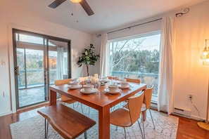 A dining area with a wooden table set for four, a potted plant, and a view through large windows. - Riverfront Dog Friendly Cabin With Mountain Views (East Stroudsburg)
