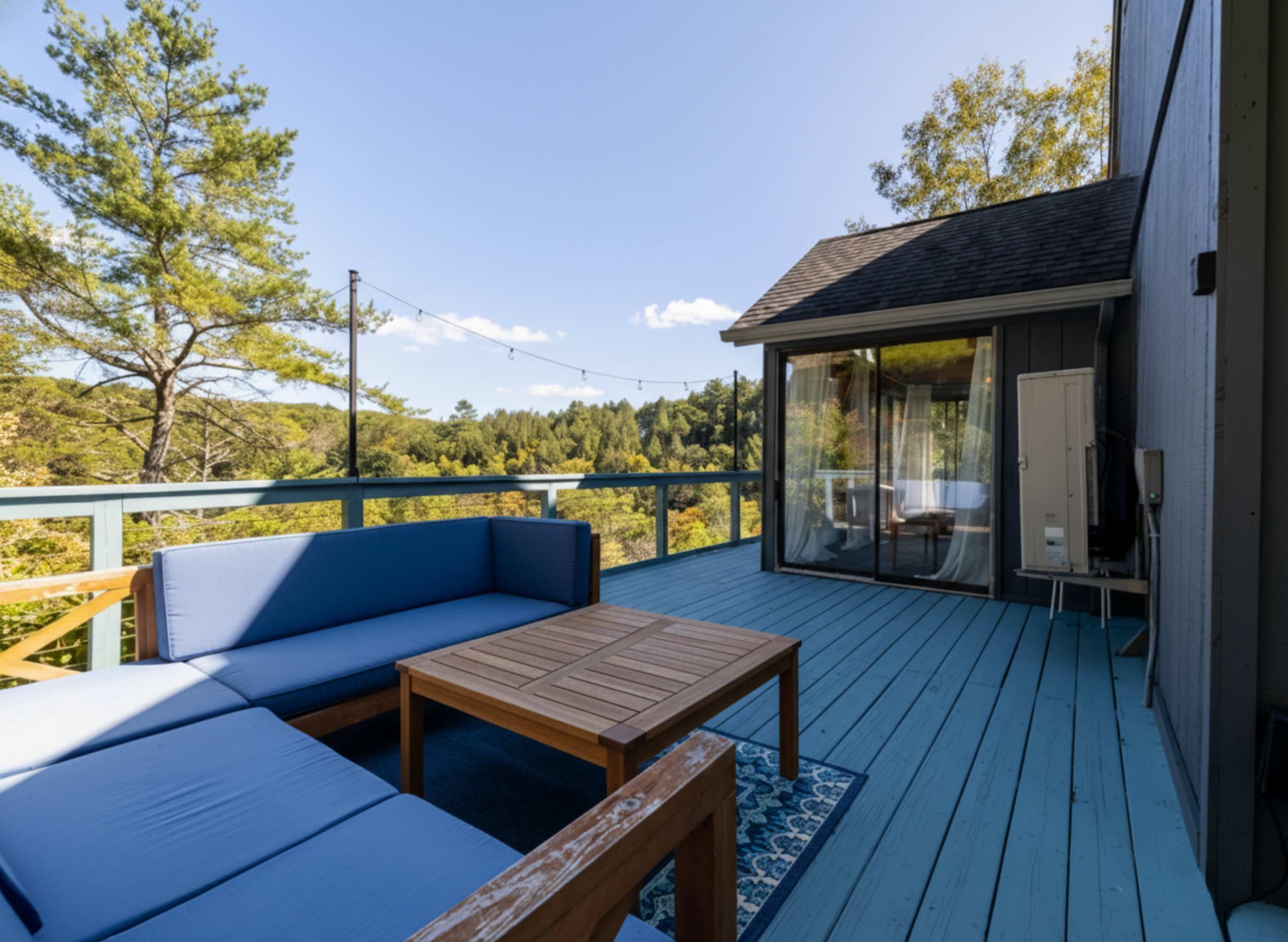 A deck with a blue sofa, wooden table, and glass doors leading to a covered area.
