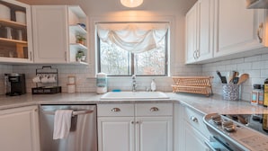 A kitchen with white cabinets, a stainless steel dishwasher, a sink with a window above, and a stove. - Riverfront Dog Friendly Cabin With Mountain Views (East Stroudsburg)