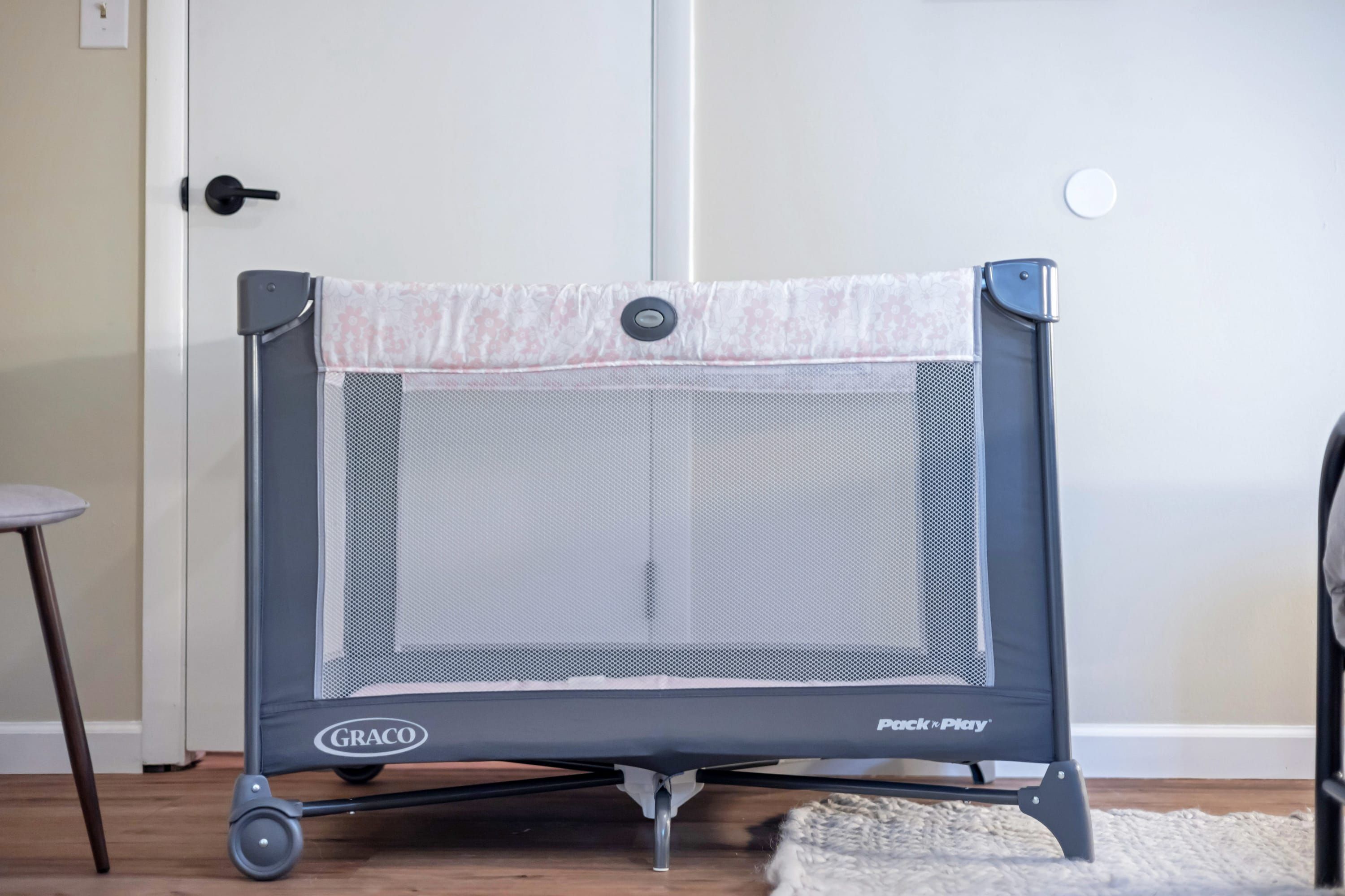A Graco trampoline with a safety net, positioned in a room with a wooden floor and a white door.