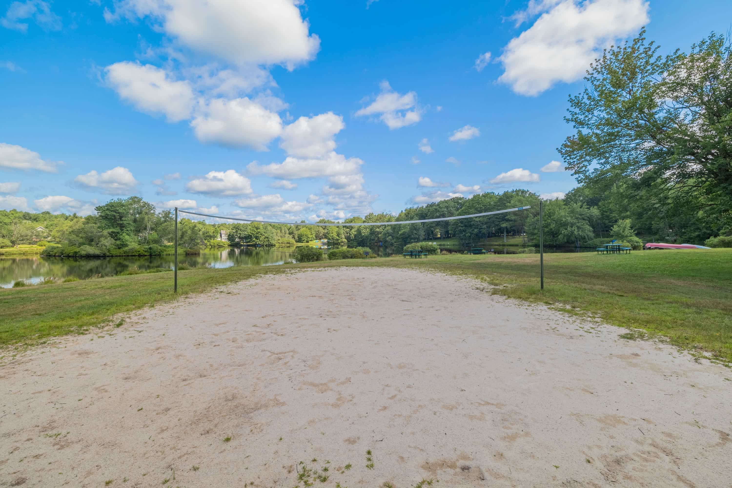 A sandy volleyball court with a net, surrounded by trees and a body of water.