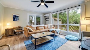 A living room with a leather sofa, a coffee table, a ceiling fan, and large windows. - Indoorpool Hottub Gameroom Firepit Dogfriendly (Long Pond)