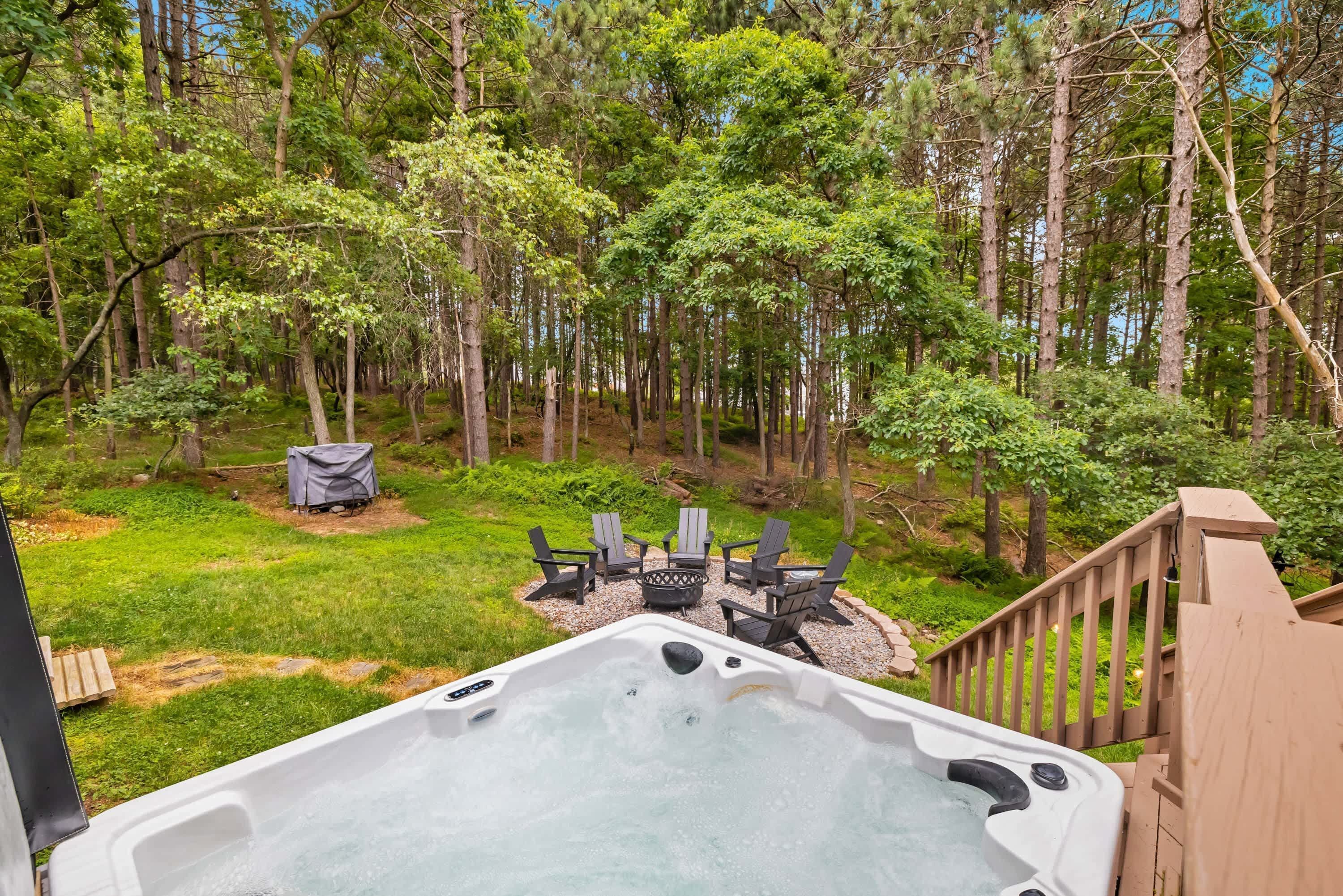 A hot tub with a deck, surrounded by a forested area and outdoor seating.