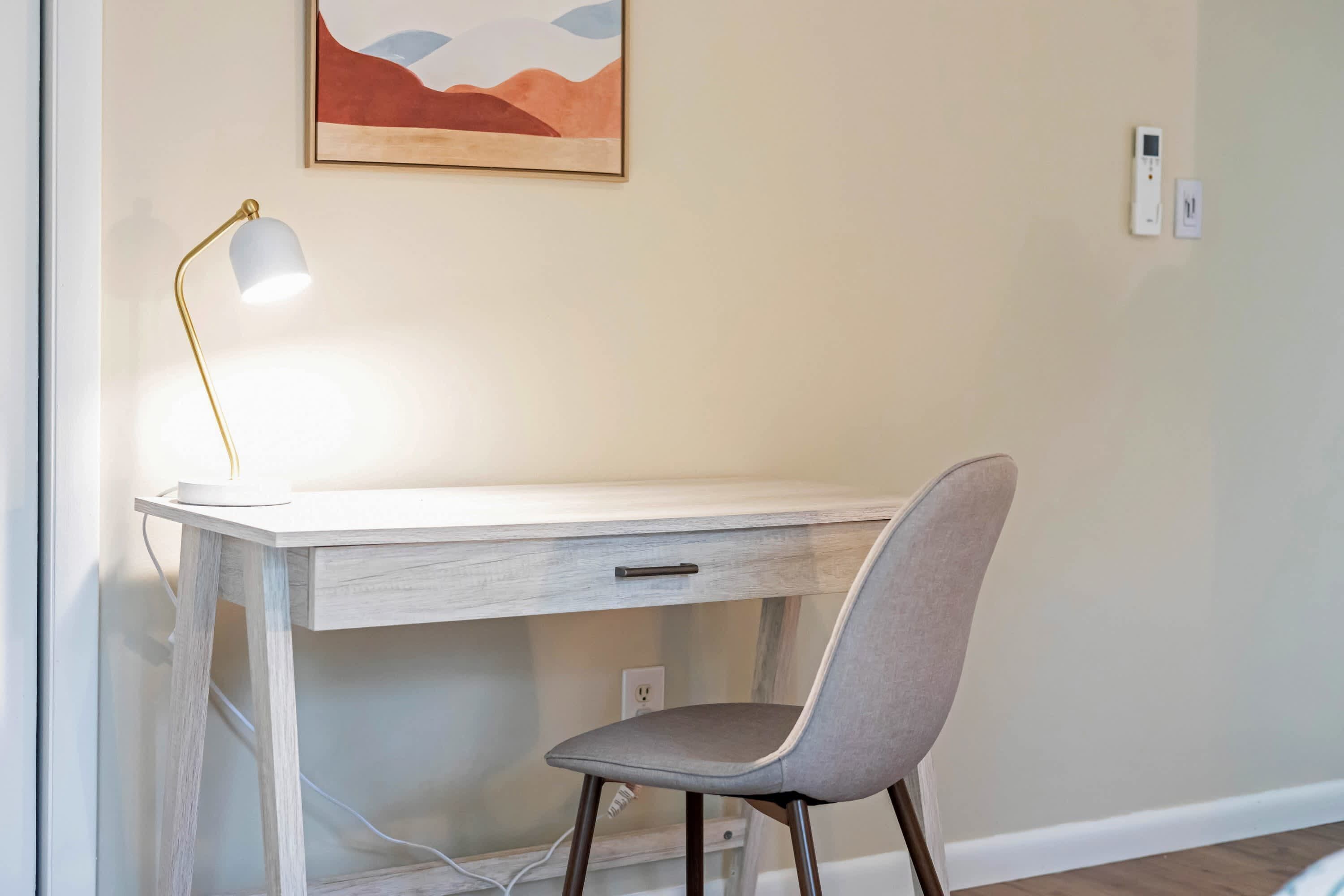 A desk with a lamp, a chair, and a wall-mounted thermostat.