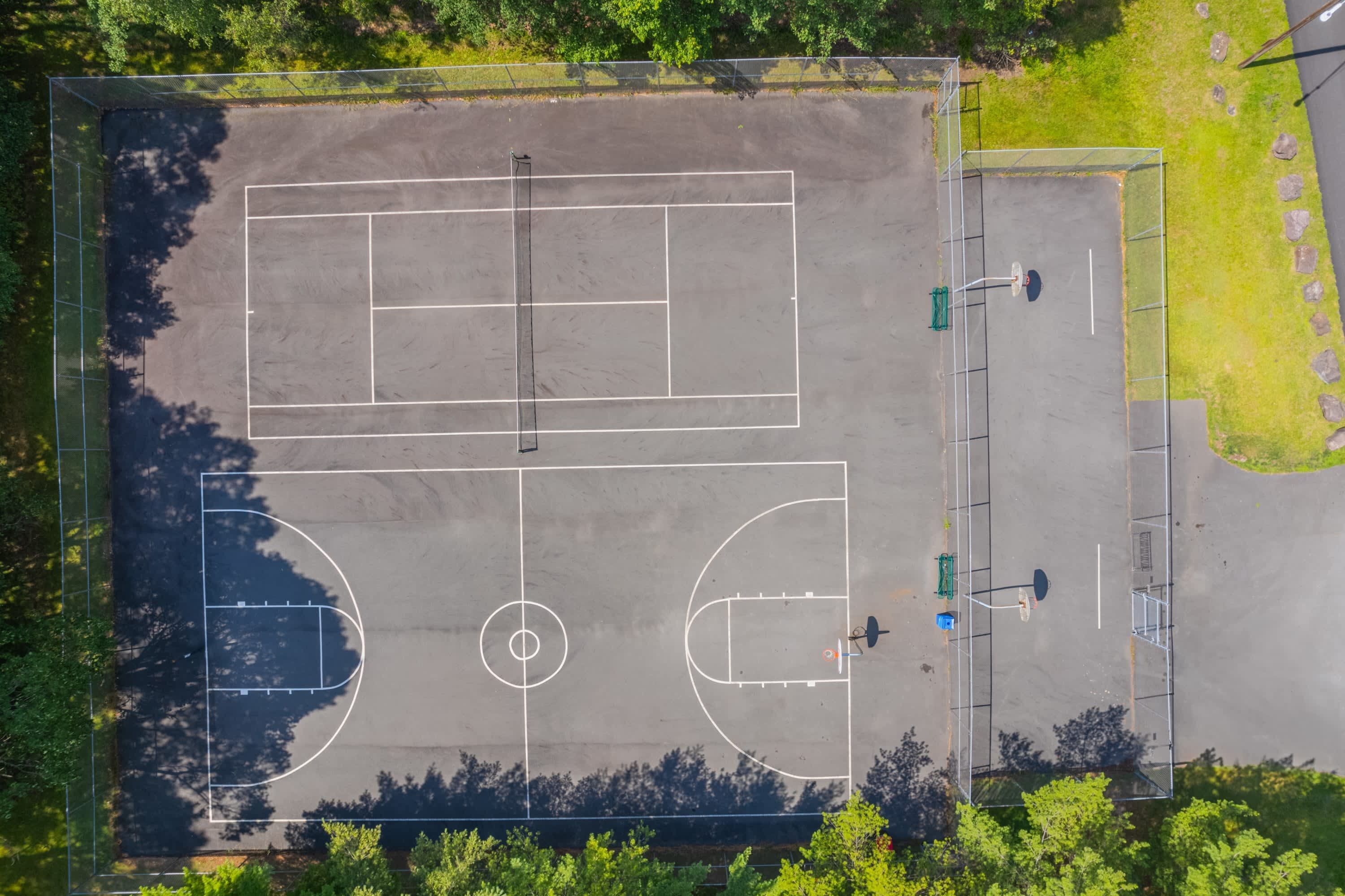 Vista aerea di un campo sportivo con canestro da basket, rete da tennis e porta da calcio.