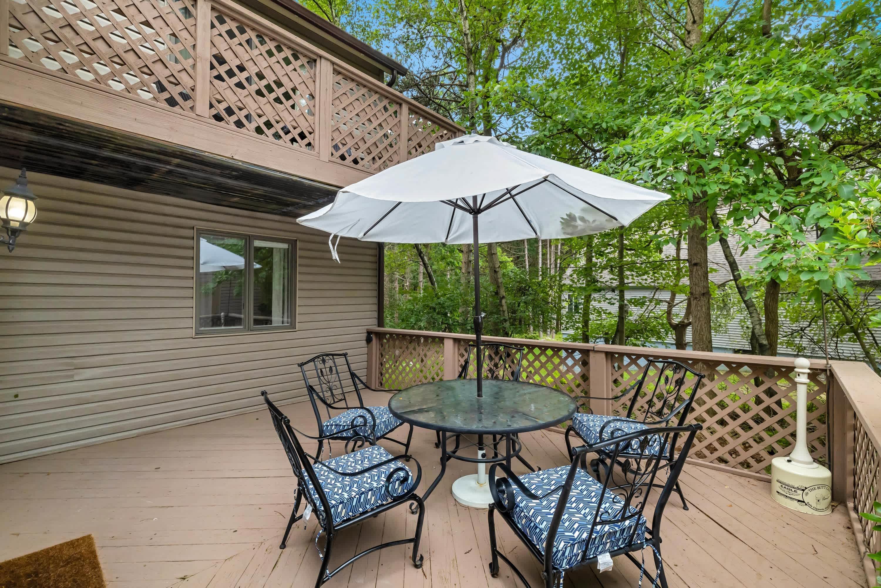 Une terrasse extérieure couverte, avec une table ronde en verre, quatre chaises et un parasol blanc.