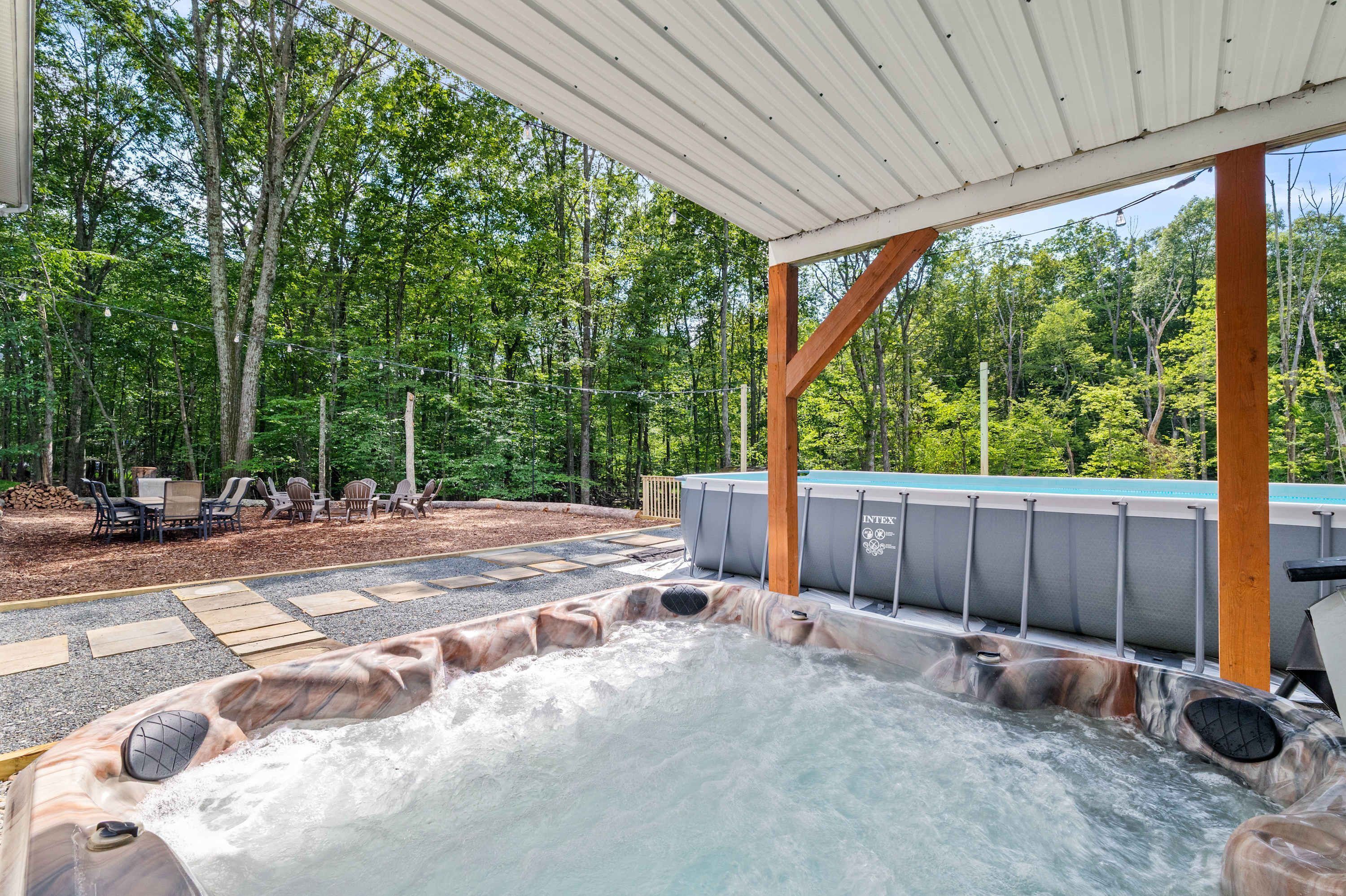 A hot tub area with a wooden deck, outdoor seating, and a pool.