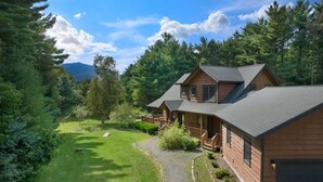 A two-story log cabin with a deck, surrounded by a well-maintained lawn and dense forest. - Whiteface Views Hot Tub Game Room Dog Friendly (Wilmington)