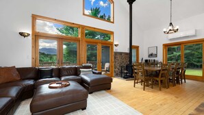 A spacious living area with a large sectional sofa, a dining table with chairs, and large windows offering views of the outdoors. - Whiteface Views Hot Tub Game Room Dog Friendly (Wilmington)