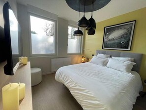 A bedroom with a bed, bedside table, two candles, a round stool, a window, and a wall-mounted artwork. - Suite "Petit Prince" - 2/4 Pers (Niergnies)