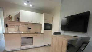 A modern kitchen with white cabinets, a wooden countertop, a built-in oven, and a flat-screen TV mounted on the wall. - Suite "Petit Prince" - 2/4 Pers (Niergnies)
