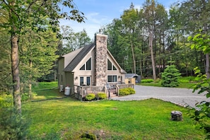 A cabin with a stone chimney, a covered porch, and a gravel driveway surrounded by trees. - Near Jfbb With Private Hot Tub and Game Room (Albrightsville)