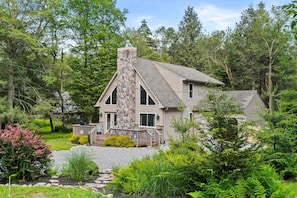 A house with a stone chimney, a deck with chairs, and a garden with various plants. - Near Jfbb With Private Hot Tub and Game Room (Albrightsville)