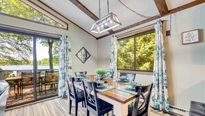 A dining area with a wooden table, black chairs, and a view of a lake. - Lakefront Poconos Retreat w Hot Tub Dog Friendly (Gouldsboro)