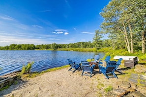 A lakeside setting with a table and chairs, a covered picnic table, and a small shed. - Lakefront Poconos Retreat w Hot Tub Dog Friendly (Gouldsboro)