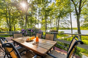 An outdoor dining area with a wooden table and chairs, surrounded by greenery and a view of a body of water. - Lakefront Poconos Retreat w Hot Tub Dog Friendly (Gouldsboro)