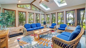 A sunroom with large windows, wicker furniture, and a ceiling fan. - Lakefront Poconos Retreat w Hot Tub Dog Friendly (Gouldsboro)