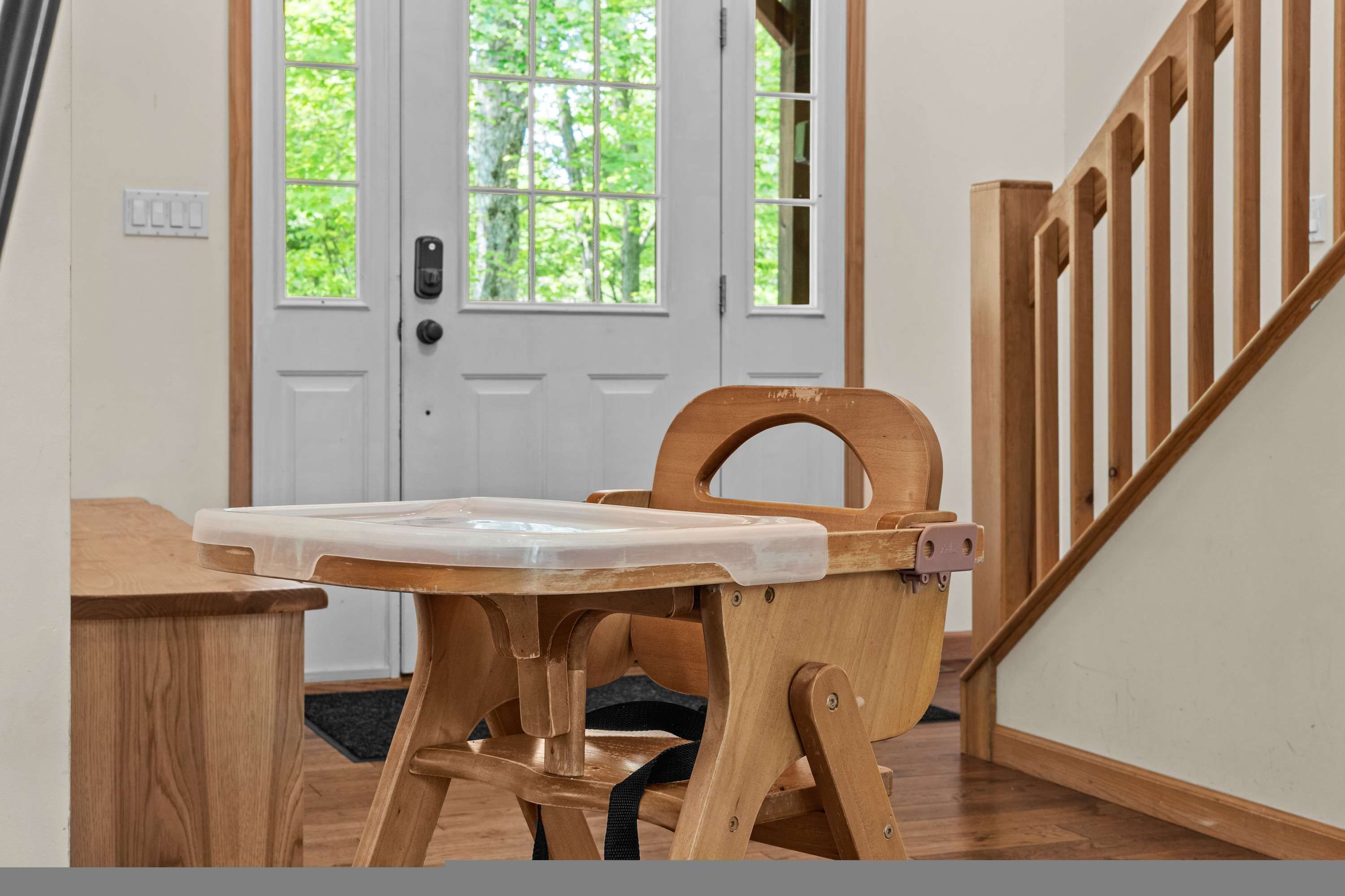 A wooden chair with a white seat, a wooden table, a white door with a window, and a wooden staircase.