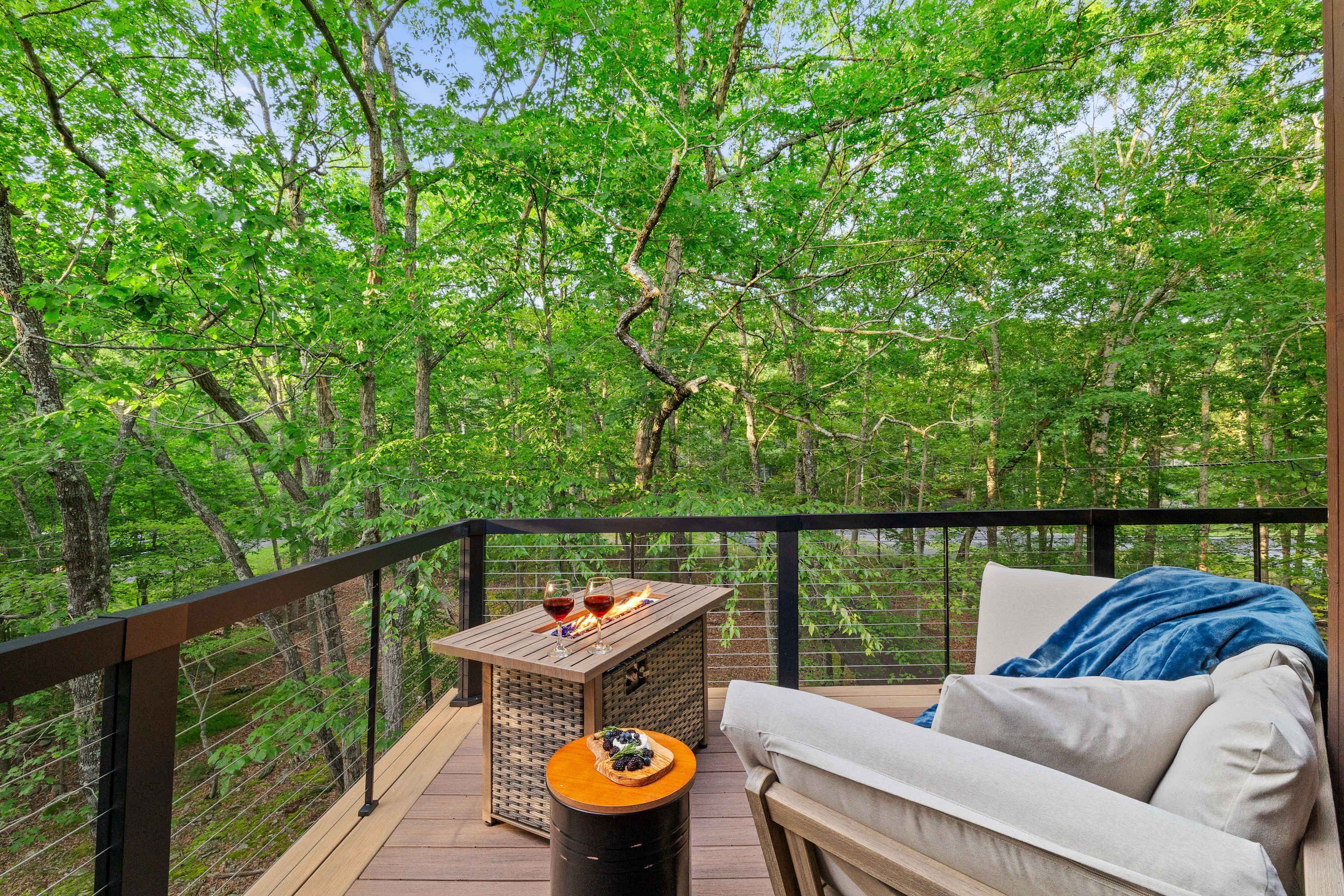 A balcony with a wooden table, a sofa, and a view of a forest.