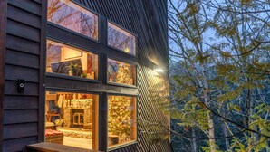 Un bâtiment moderne doté de nombreuses fenêtres, d’une cheminée en pierre et offrant une vue sur les arbres.