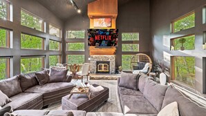 Un salon moderne avec une cheminée en pierre, de grandes fenêtres et un écran pour regarder Netflix.