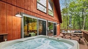 A wooden deck with a hot tub, outdoor seating, and a view of a forested area. - Dog-friendly Pocono Chalet w Hot Tub Indoor Pool (Long Pond)