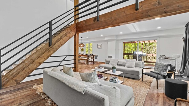 A spacious living area with a staircase, a sofa, a coffee table, and a dining area. - Dog-friendly Pocono Chalet w Hot Tub Indoor Pool (Long Pond)