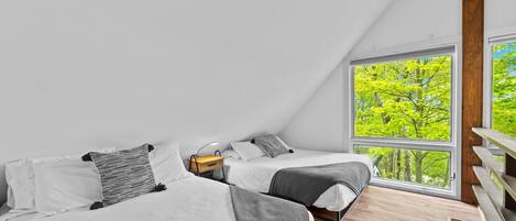 Un dormitorio moderno con dos camas, piso de madera y un ventanal con vistas a árboles.