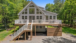 A two-story house with a deck, surrounded by trees. - Game Room A C Dog-friendly Stay With Hot Tub (Albrightsville)