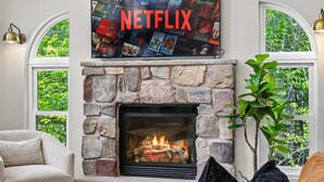 A stone fireplace with a fire, a wall-mounted Netflix sign, and a window with a view of greenery. - Game Room A C Dog-friendly Stay With Hot Tub (Albrightsville)