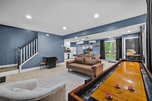 A living room with a shuffleboard table, a sofa, a coffee table, and a staircase. - Game Room A C Dog-friendly Stay With Hot Tub (Albrightsville)