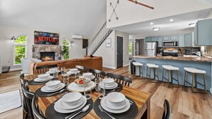 A modern living room with a fireplace, dining area, kitchen, and a staircase leading to another level. - Game Room A C Dog-friendly Stay With Hot Tub (Albrightsville)