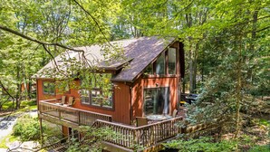 Eine Hütte mit einer Terrasse, einem Kamin und Blick auf den Wald.