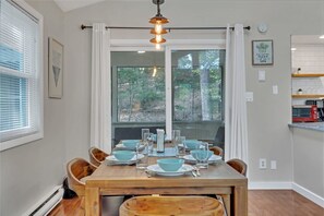 A dining area with a wooden table set for four, a hanging light fixture, and a view of the outdoors through large windows. - Slopeside Lounge Gameroom Lakes Pools Dogs Welcome (Bushkill)