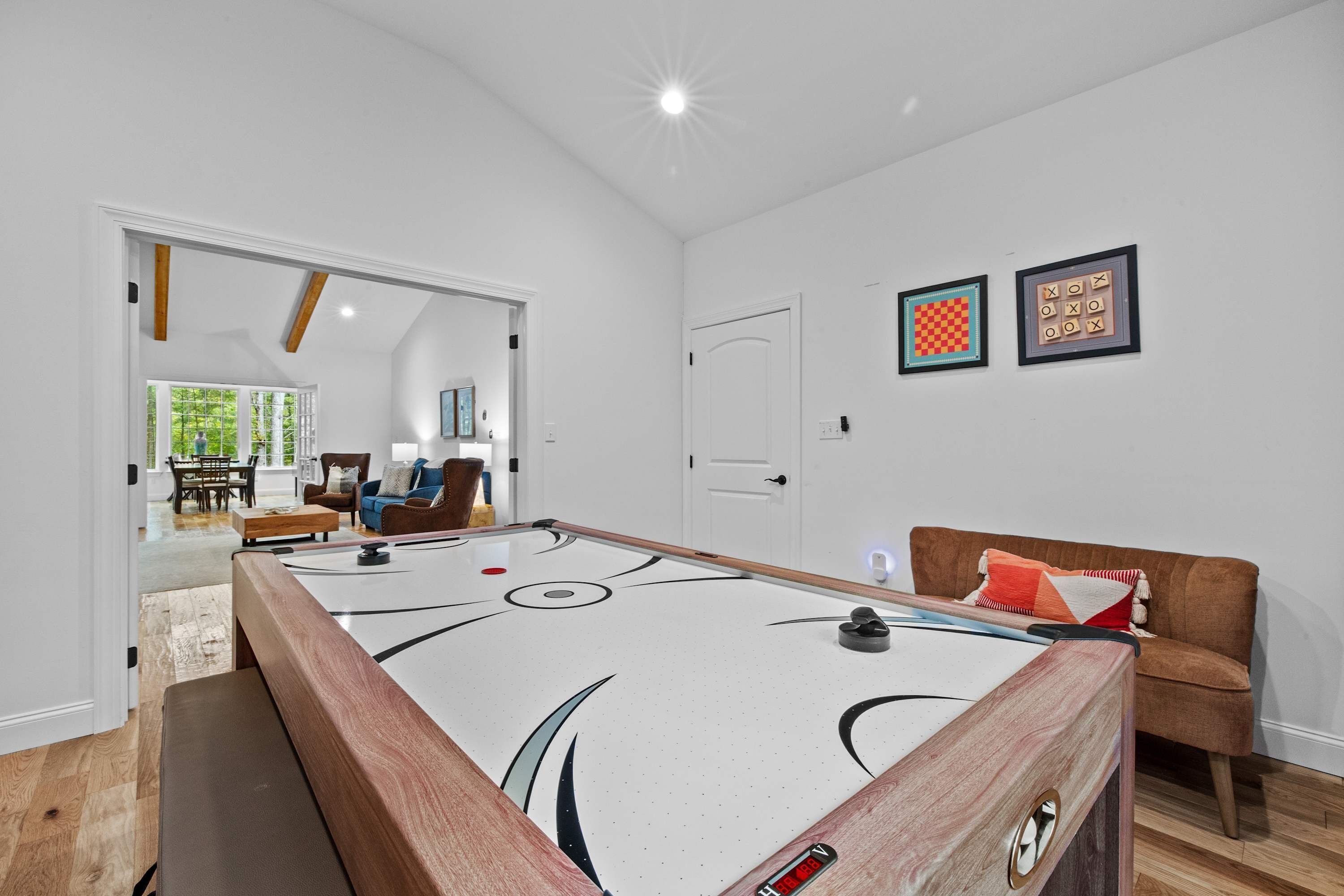 A pool table in a room with a wooden bench, a brown sofa, and a door leading to another room.