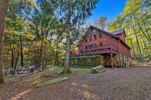 Uma cabana com base de pedra, fachada vermelha e varanda com vista para uma área arborizada.
