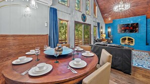 A dining area with a round table set for six, a fireplace, and a large window with a view of trees. - Poconos Speakeasy Hot Tub Dog-friendly Near Ski (Lake Harmony)