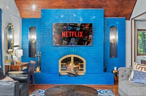 Uma sala de estar com lareira de tijolos azuis, uma televisão montada exibindo a interface da Netflix, e uma decoração com tema de cisne.