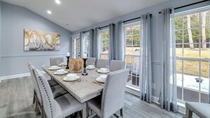 Ein Esszimmer mit einem großen Tisch, gedeckt für sechs Personen, umgeben von Stühlen, mit einem Gemälde an der Wand und Blick ins Freie durch große Fenster.
