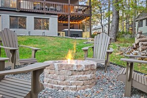 A fire pit surrounded by Adirondack chairs, a deck with string lights, and a view of a house with a balcony. - Streamside Hot Tub Dog Friendly Resort Access (Pocono Lake)