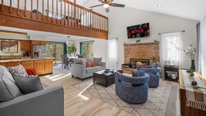 A spacious living area with a high ceiling, a fireplace, and a kitchen in the background. - Streamside Hot Tub Dog Friendly Resort Access (Pocono Lake)