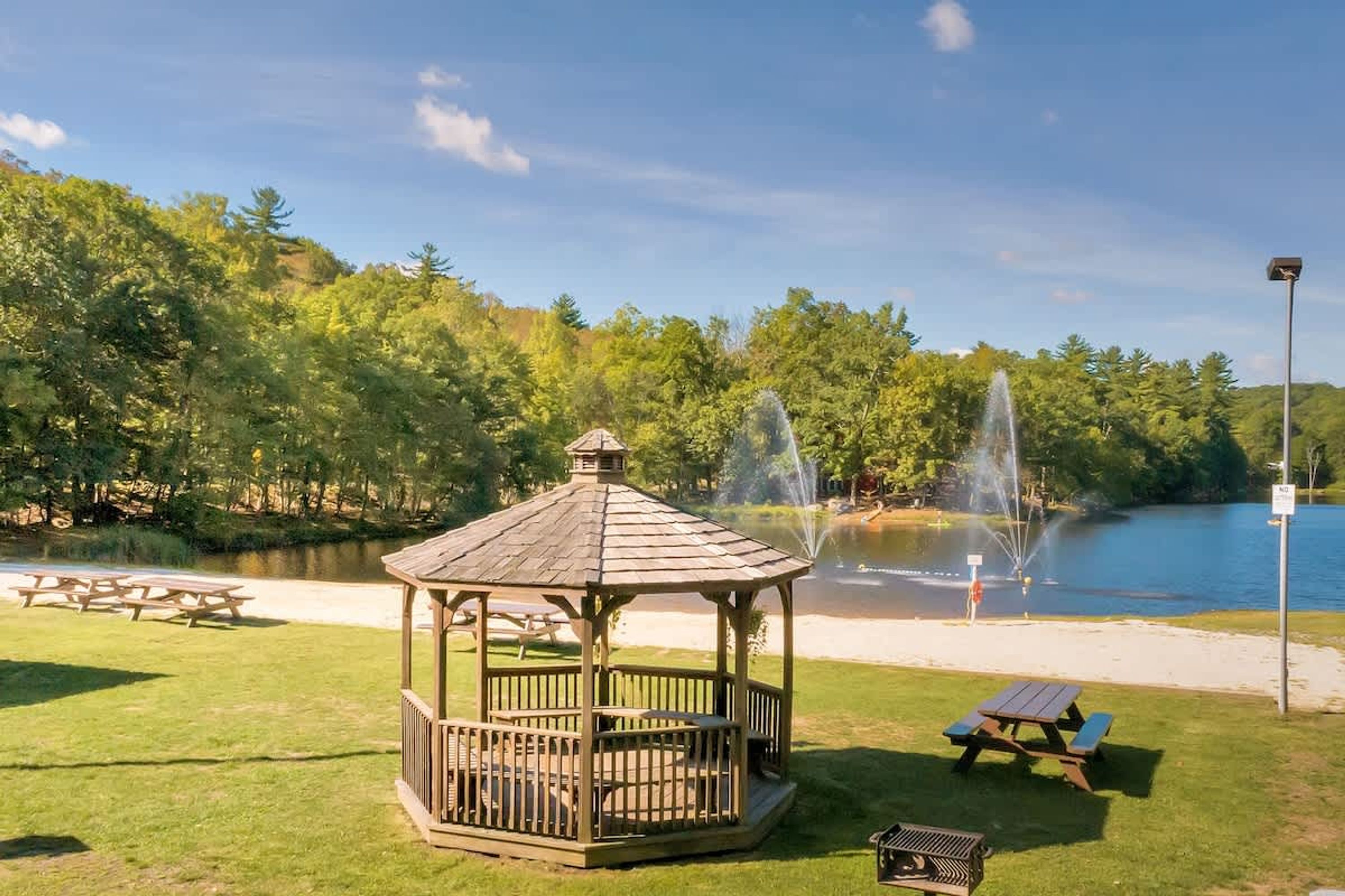A gazebo with picnic tables, a pond with fountains, and a clear sky.