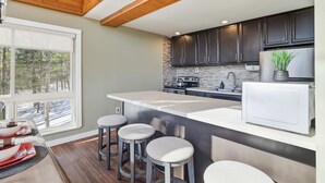 A modern kitchen with dark cabinets, a large island with stools, a white refrigerator, and a window with a view of trees. - Views of Blue Mountain Near App Trail Game Room (Palmerton)