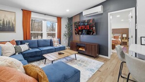 A modern living room with a blue sofa, a fireplace, a large TV wall, and a door leading to another room. - Amenity-filled Retreat by Jfbb-pickleball-gameroom (Albrightsville)