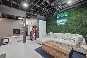 A modern interior with a green wall, a neon sign, a sofa, a coffee table, and a basketball arcade. - Amenity-filled Retreat by Jfbb-pickleball-gameroom (Albrightsville)