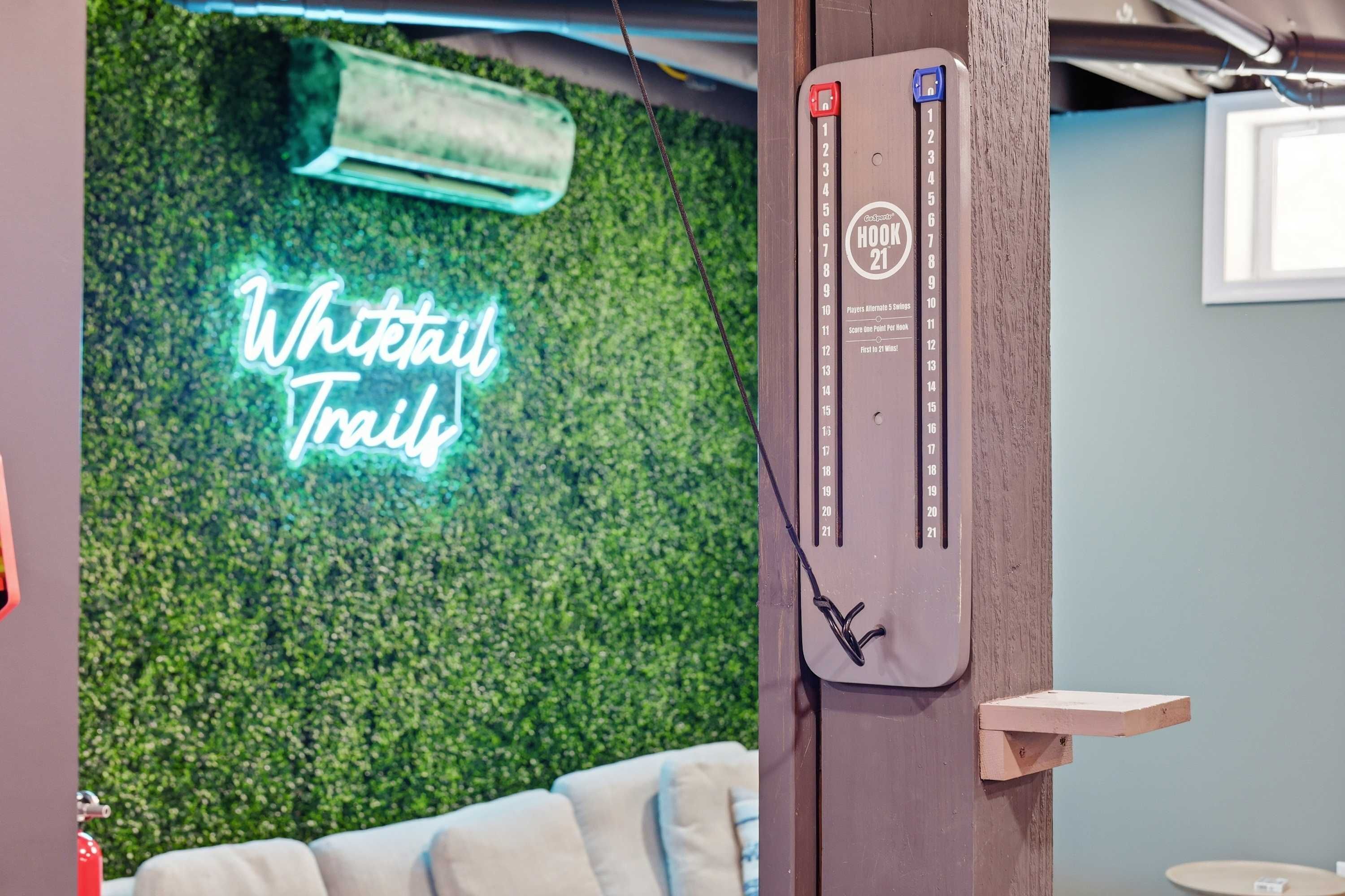 A room with a neon sign reading 'Whitetail Trails,' a wooden wall, a small wooden shelf, and a wall-mounted device.